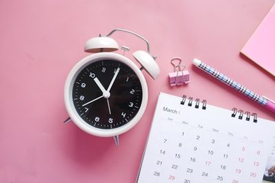 Ein Wecker neben einem Kalender und Schreibutensilien – erinnert daran, wie wichtig es ist, TMS-Anmeldefristen pünktlich im Blick zu behalten.
