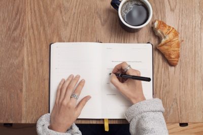 Person füllt eine Checkliste am Frühstückstisch aus – perfekte Vorbereitung für den TMS-Testtag mit Kaffee und Croissant.