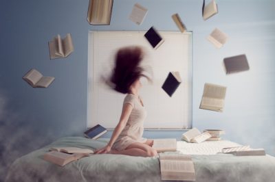 Studienbewerberin sitzt auf Bett, Bücher fliegen durch die Luft – Sinnbild für den Stress vor Prüfungen wie dem TMS